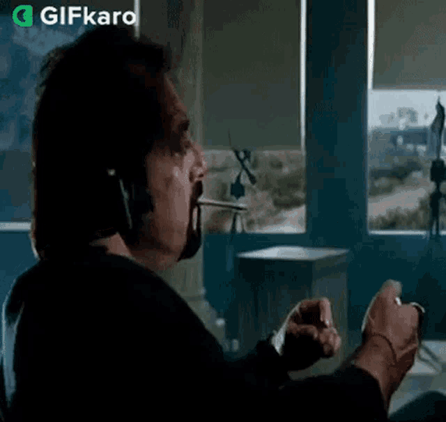 a man wearing headphones is smoking a cigarette in front of a window with gifkaro written in the corner