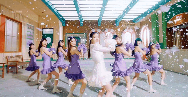 a group of girls in purple dresses are dancing in a room with snow falling around them .