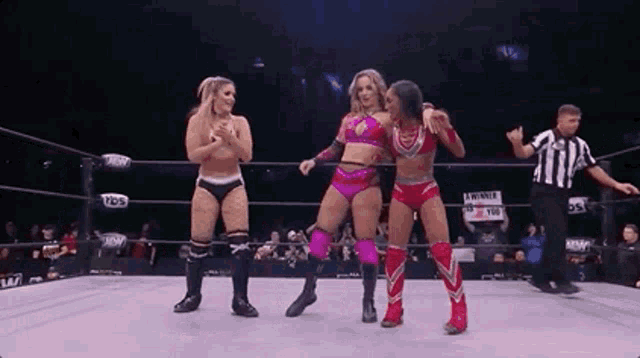three women are standing in a wrestling ring with a referee .