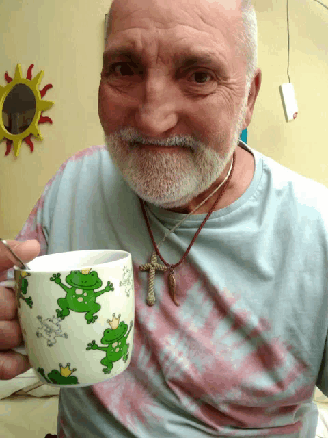 a man in a tie dye shirt holds a cup with frogs on it