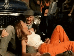 a man and a woman are laying on the ground in front of a car