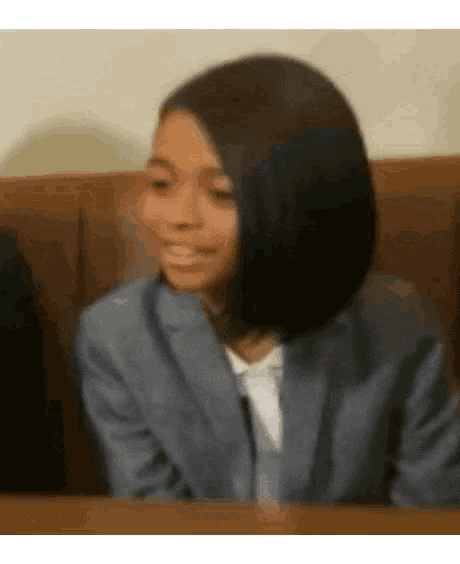 a woman in a suit is sitting at a table making a face .