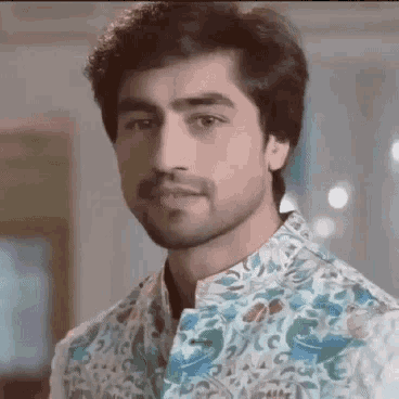 a close up of a man with a beard wearing a floral shirt and looking at the camera .