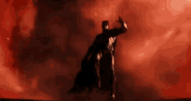a man in a black cape is standing in front of a red sky .