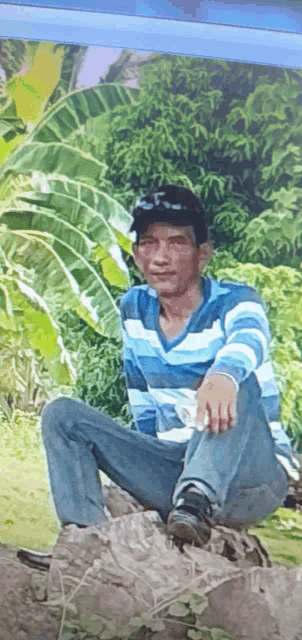 a man in a blue striped shirt sits on a rock