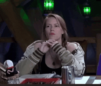 a woman is sitting at a table in a dark room holding a cigarette .