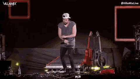 a man in a baseball cap is dancing on a stage in front of a guitar .