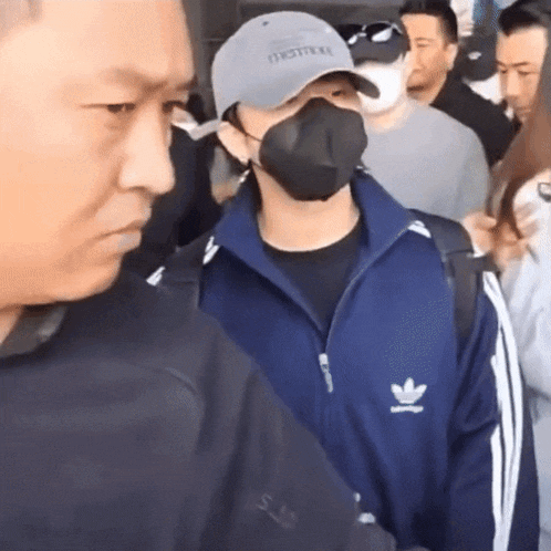 a man wearing a mask and an adidas jacket stands in a crowd of people