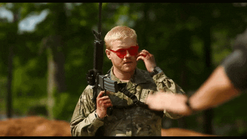 a man in a military uniform is holding a rifle and wearing red sunglasses