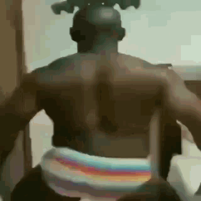 a man without a shirt is dancing in a room while wearing rainbow colored underwear .