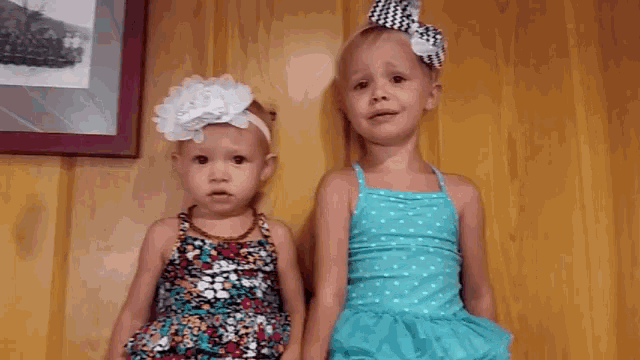 two little girls are standing next to each other in front of a wall .