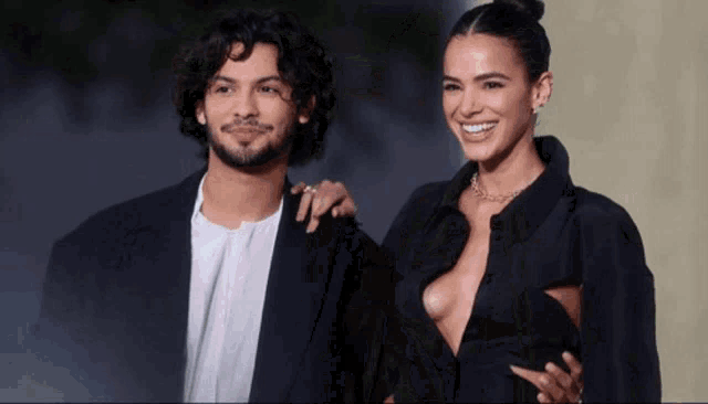 a man and a woman are posing for a picture and the woman is wearing a plunging black dress