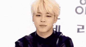 a young man with blonde hair is making a funny face while wearing a black shirt and a black jacket .