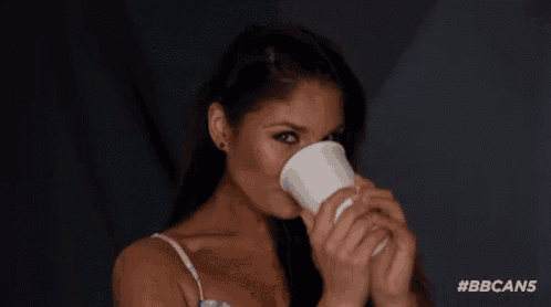 a woman is drinking from a white cup and smelling it .