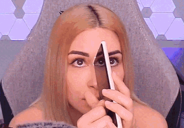 a woman with blonde hair is holding a pencil to her face
