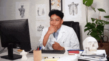 a man in a lab coat sits at a desk in front of a computer monitor