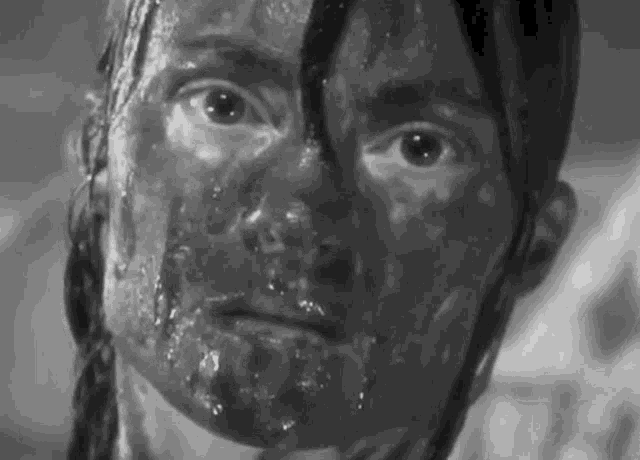 a black and white photo of a woman 's face covered in mud