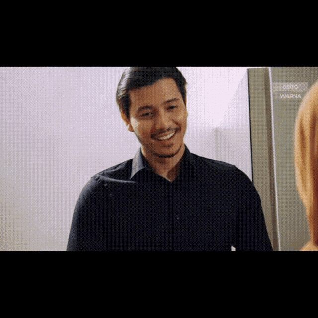 a man in a black shirt is smiling while standing in front of a fridge .