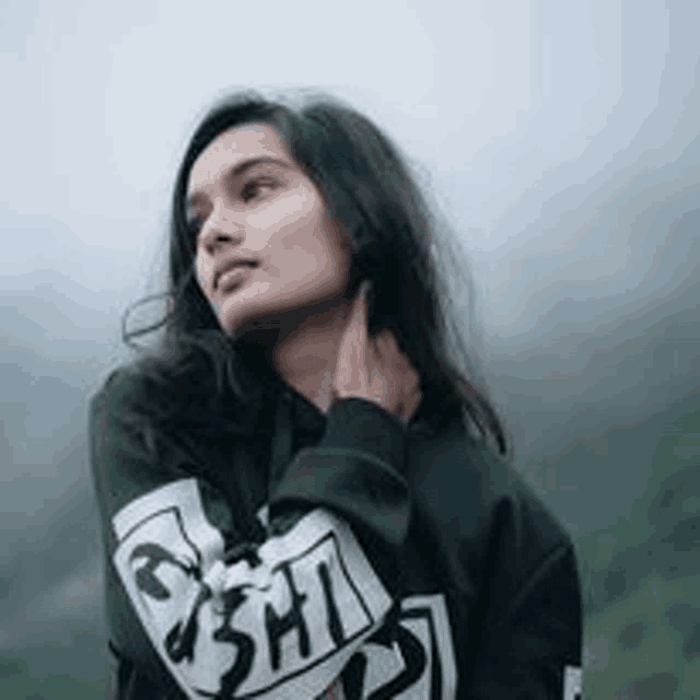 a woman in a black sweatshirt is standing in front of a foggy mountain .