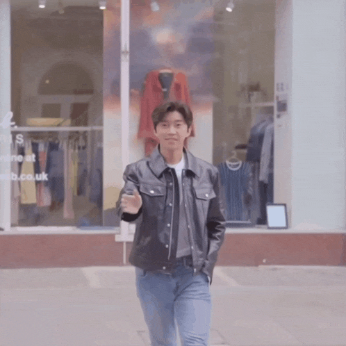 a man in a leather jacket is waving in front of a store window that says ' s ' on it