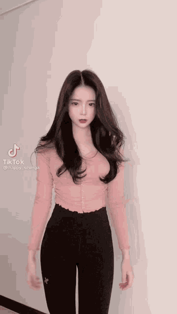 a girl with long black hair is wearing a pink shirt and black pants .