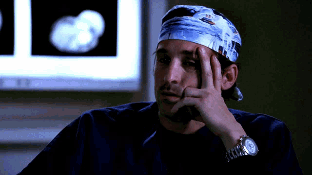 a man wearing a blue scrub cap and a watch has his hand on his forehead