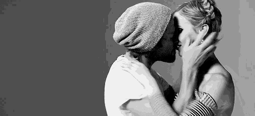 a black and white photo of a man and woman kissing .