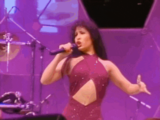 a woman in a purple dress is singing into a microphone on stage .