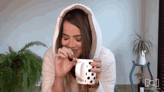 a woman wearing a hooded robe is drinking from a white mug