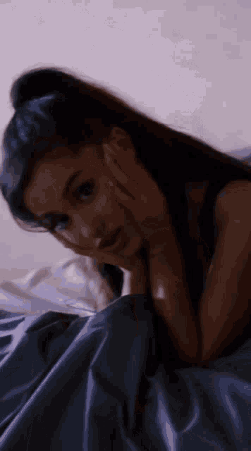a woman laying in bed with her hand on her face