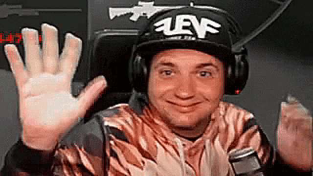 a man wearing headphones and a hat is sitting in a chair and waving .