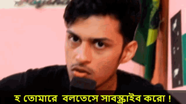 a man with a beard is talking into a microphone with a foreign language written below him