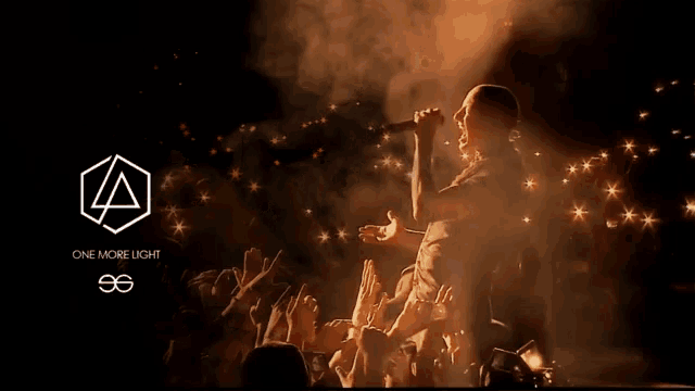 a man singing into a microphone in front of a crowd with a one more light logo