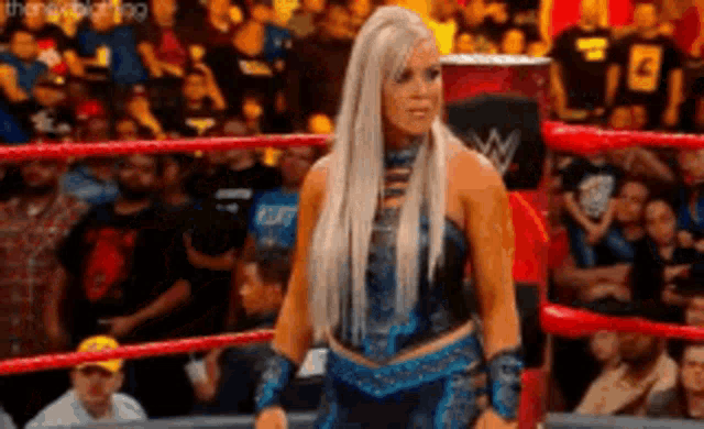 a woman in a blue dress is standing in a wrestling ring in front of a crowd .