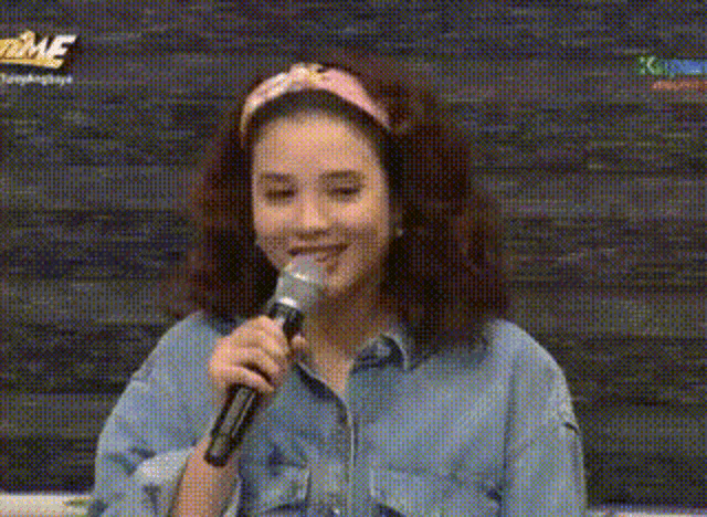 a woman is smiling while holding a microphone in front of a wall .
