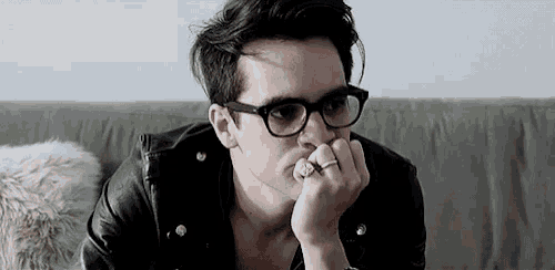 a man wearing glasses and a leather jacket is sitting on a couch with his hand on his chin .