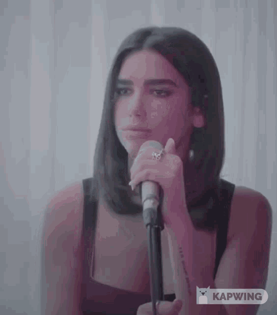 a woman singing into a microphone with a ring on her finger