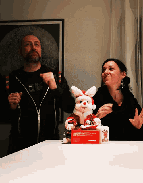 a man and a woman are standing next to a stuffed bunny wearing a santa hat