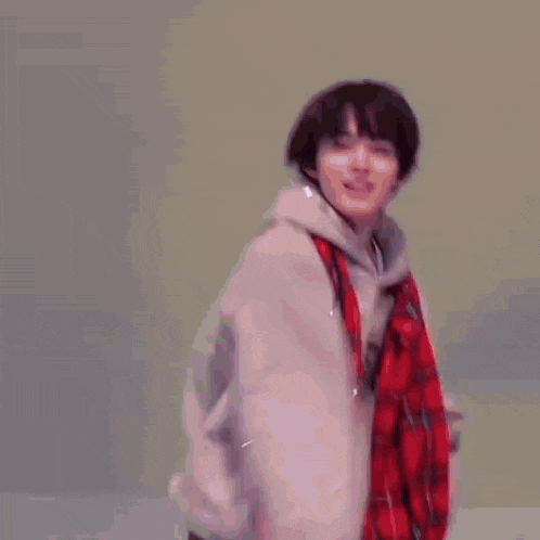 a young man wearing a hoodie and a plaid scarf is dancing in a room .
