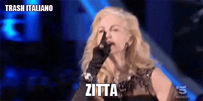 a woman in a black dress is making a gesture with her finger and the word zitta is above her