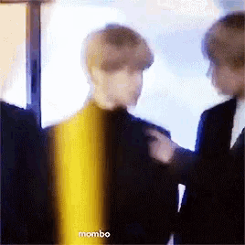 a blurry picture of two men standing next to each other with the words mombo on the bottom right