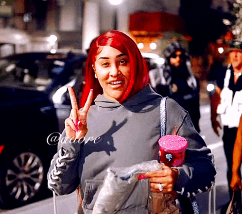a woman with red hair is wearing a grey hoodie and making a peace sign