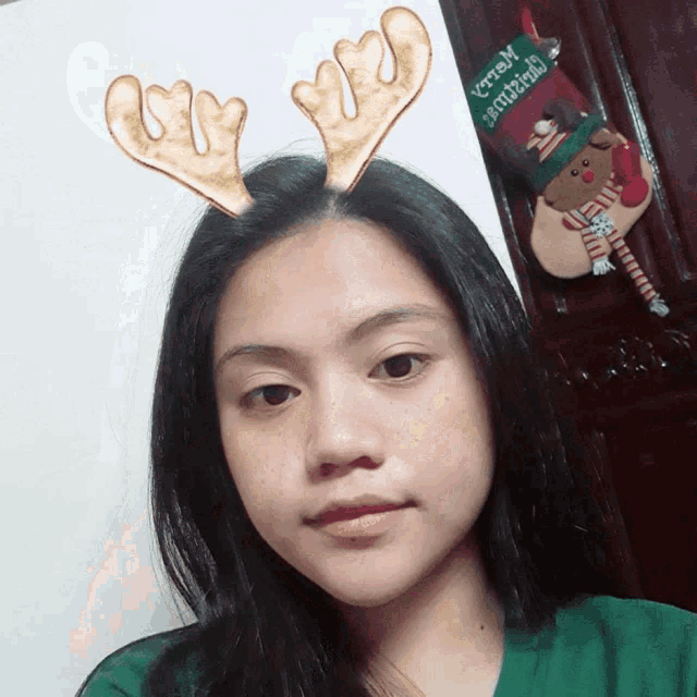 a woman wearing reindeer antlers stands in front of a christmas decoration