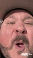 a close up of a man with a beard wearing a cowboy hat making a funny face .