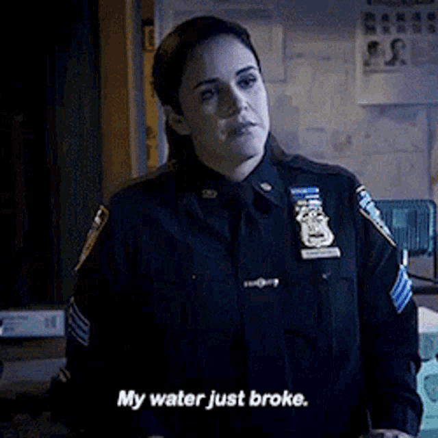 a woman in a police uniform is standing in a dark room and saying `` my water just broke . ''