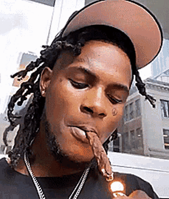 a man with dreadlocks is smoking a cigarette while wearing a hat .