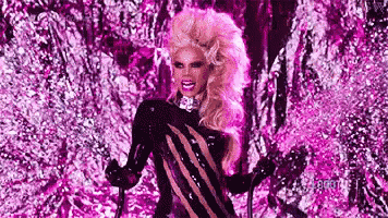 a drag queen is standing in front of a purple background .
