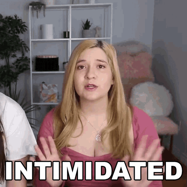 a woman in a pink shirt says intimidated in front of a shelf