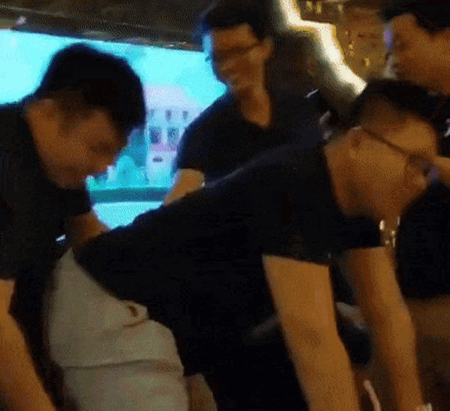 a group of men are standing around a table and one of them has glasses on .