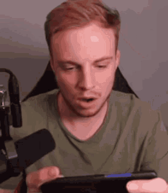 a man is sitting in front of a microphone while playing a video game on a tablet .